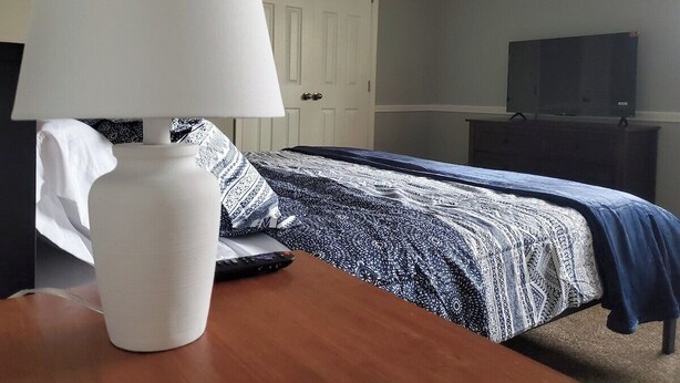 Une chambre à coucher avec un lit, une table de chevet avec une lampe, une commode et un téléviseur.