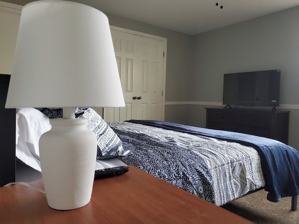 A bedroom with a bed, a bedside table with a lamp, a dresser, and a television.