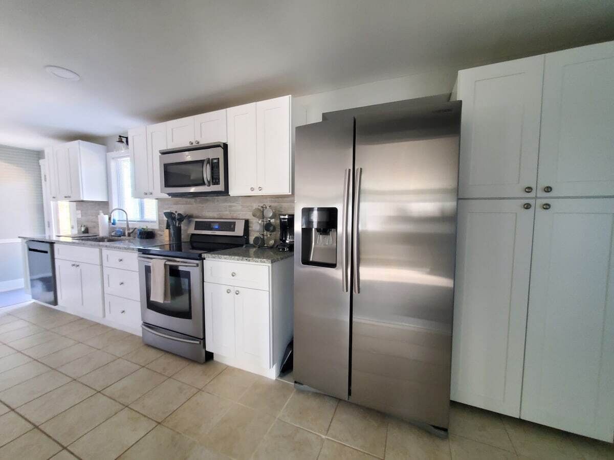 A modern kitchen with stainless steel appliances, white cabinetry, and a tiled floor.