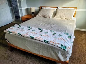 A bed with a patterned bedspread and pillows, a bedside table with a lamp, and a door in the background.