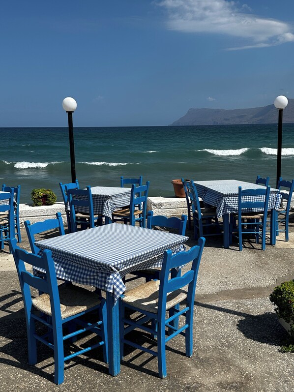 Un área de estar al aire libre con sillas y mesas azules, con vista al mar.