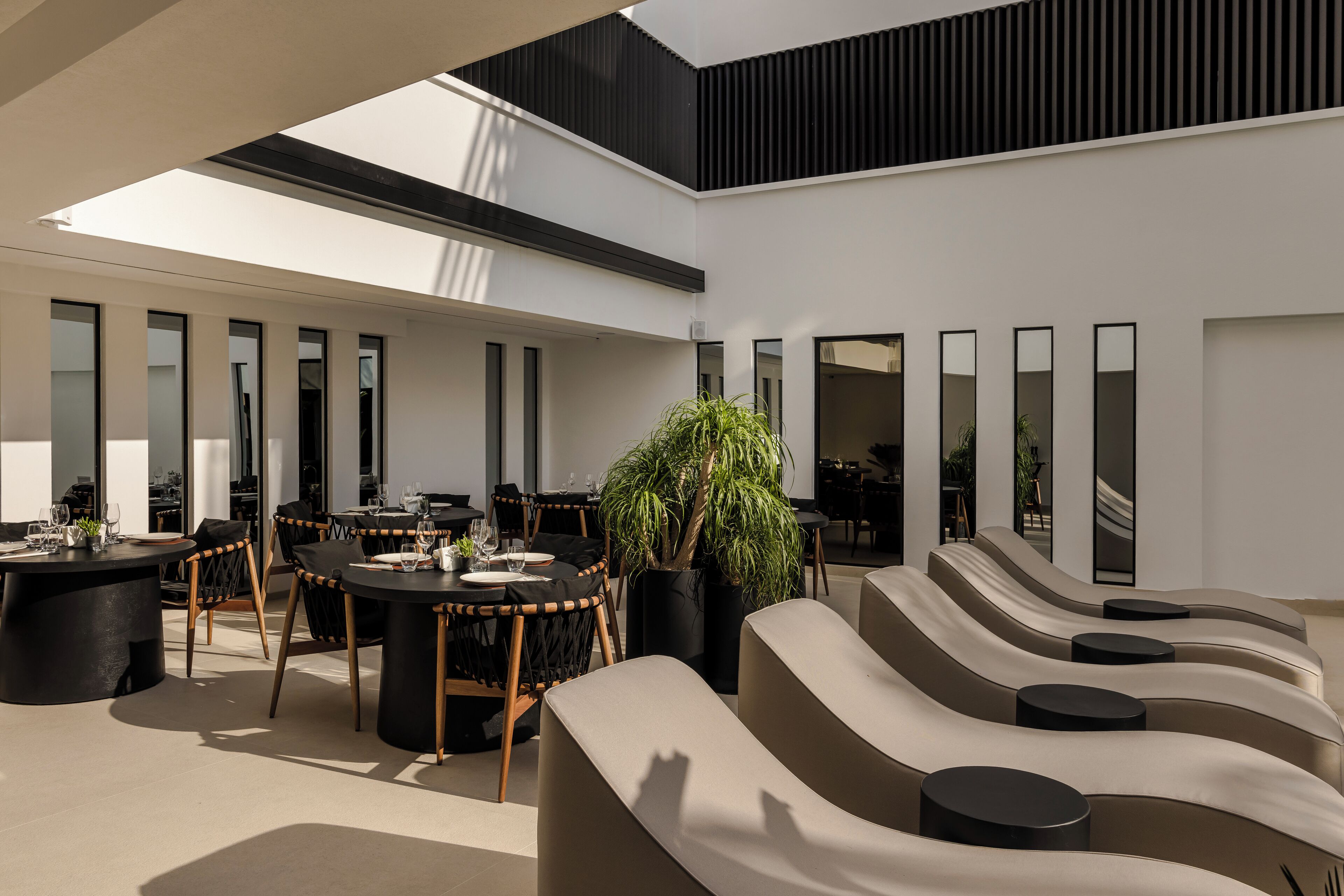 A modern outdoor dining area with round tables and chairs, a large potted plant, and a seating area with curved sofas and round tables.