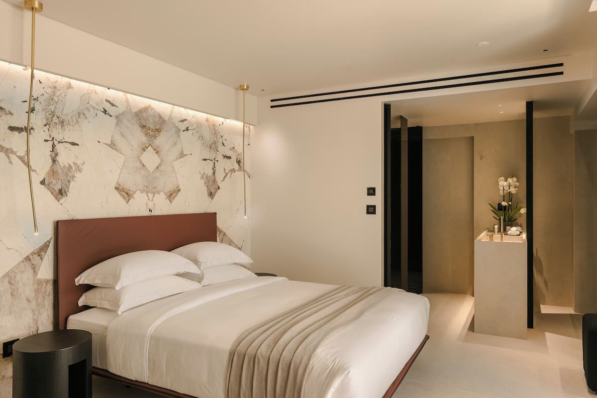 A modern bedroom with a marble headboard, a large bed with white linens, a bedside table, and a nightstand.
