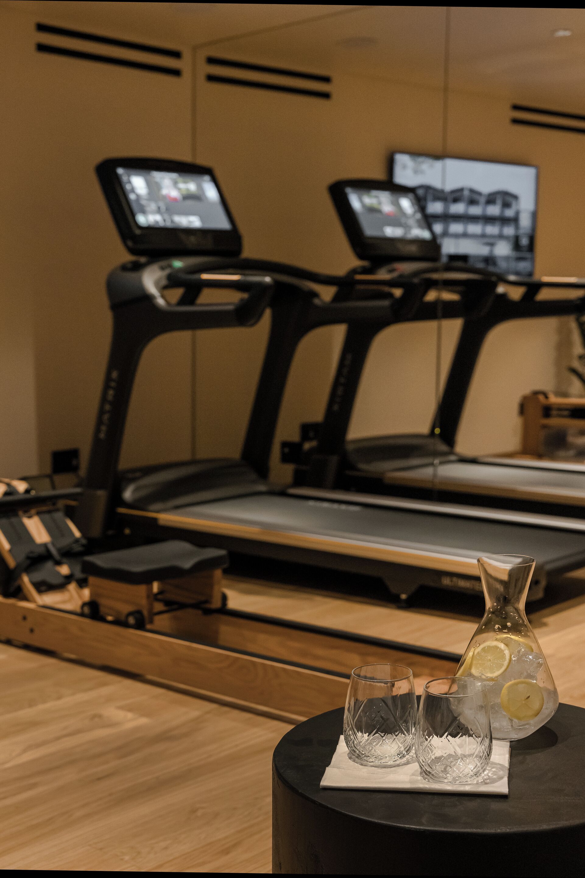 A gym with treadmills, a water dispenser, and two glasses on a table.