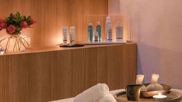 A modern spa room with a wooden reception desk, a vase of flowers, and a tray with towels and candles.