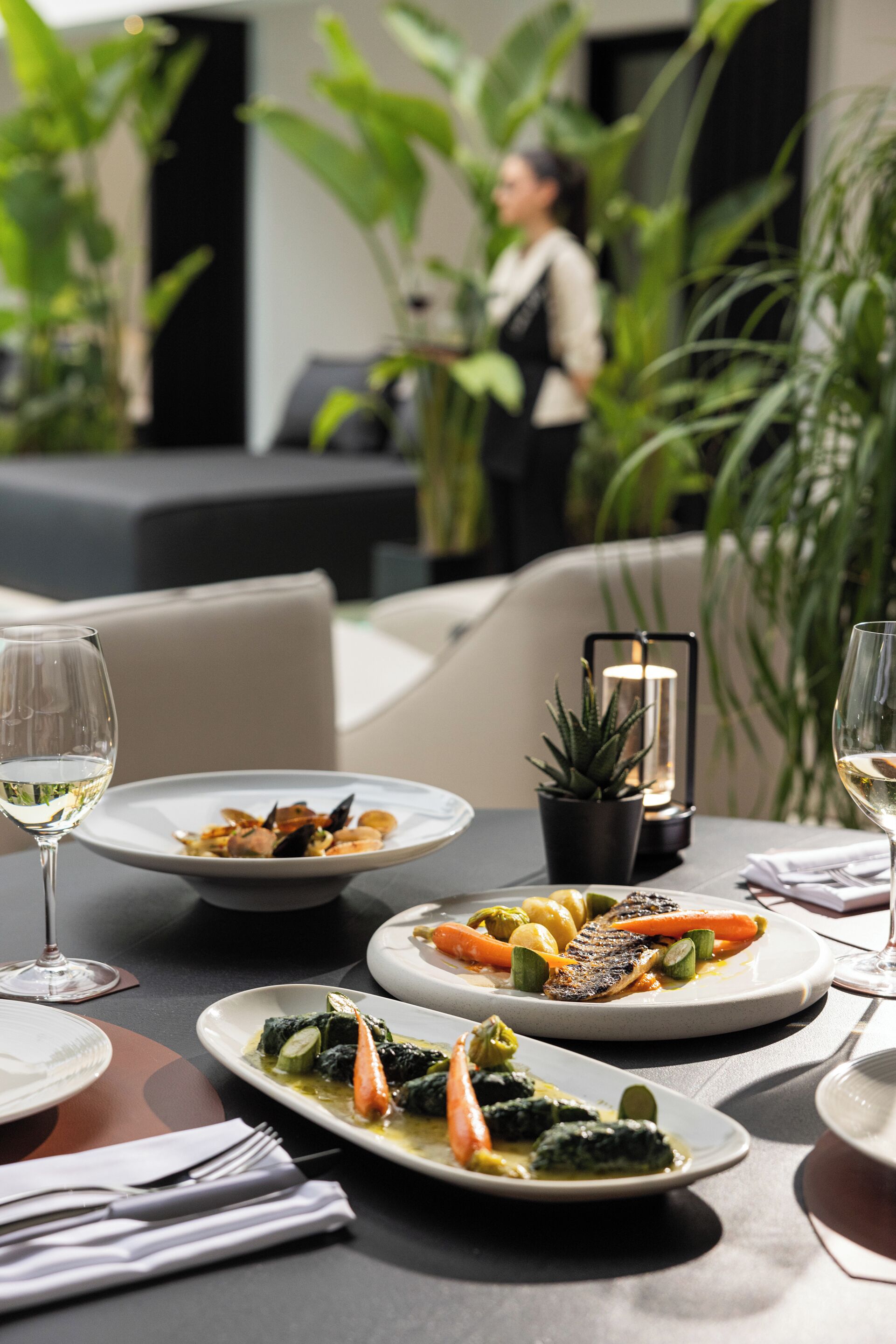 A dining table with plates of food, glasses of wine, and a lit candle centerpiece.