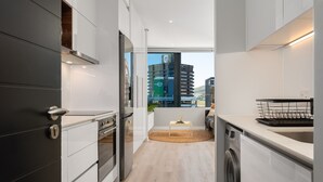 A modern kitchen with a built-in oven, a washing machine, and a large window offering a view of the city. - Modern 16 On Bree Apartment , No Loadshedding (Cape Town)