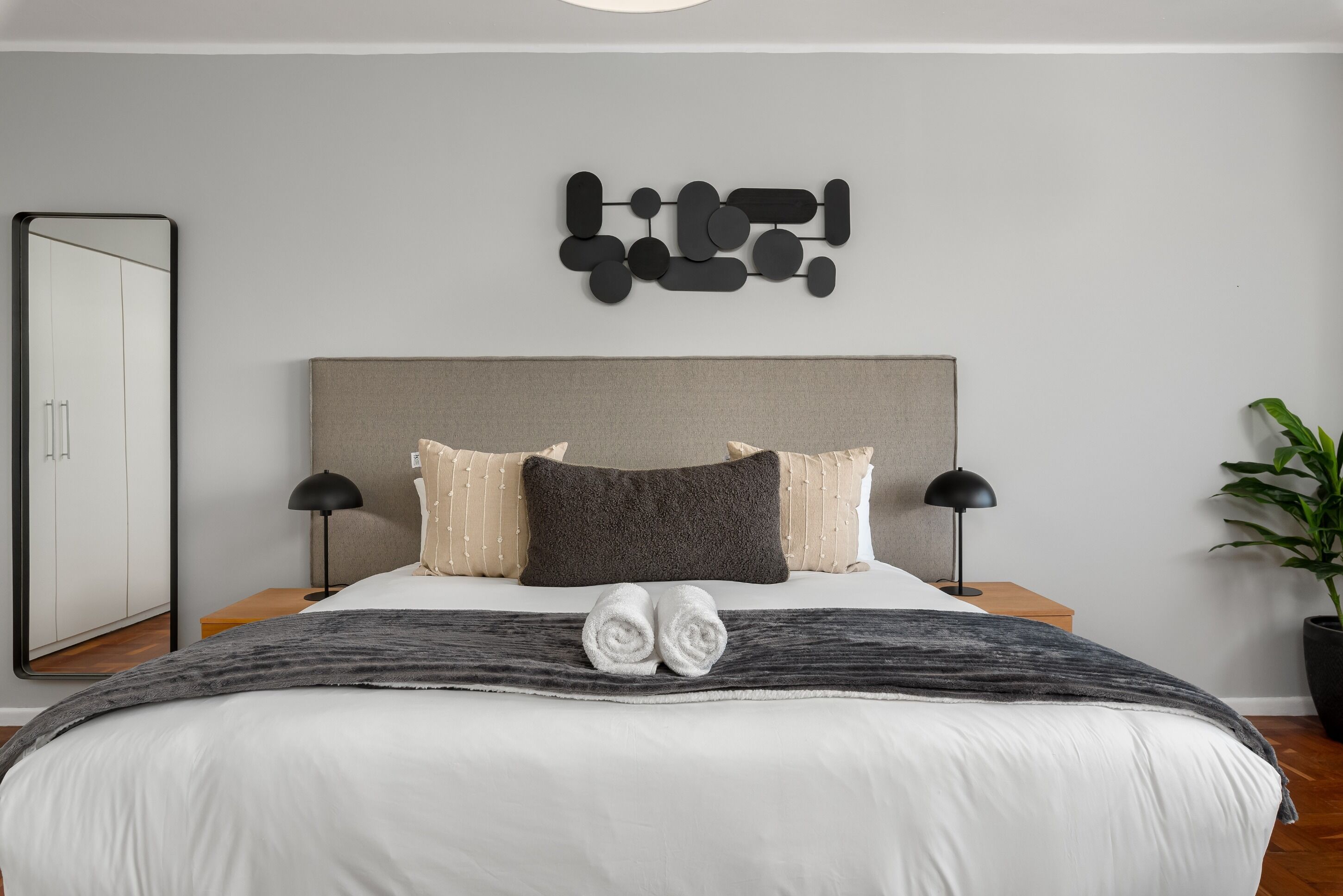 A modern bedroom with a large bed, two bedside tables, a wall art piece, and a potted plant.