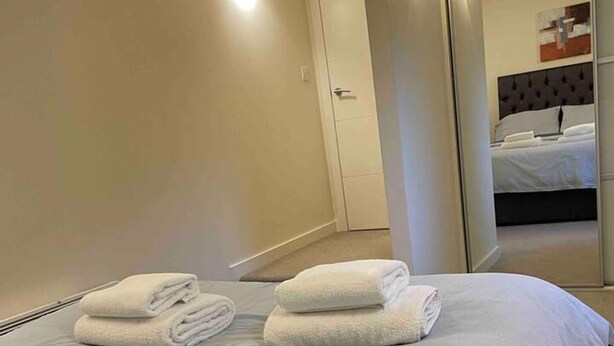 Habitación de hotel con cama bien hecha, una puerta y un espejo que refleja una cama y una pared con interruptor de luz.