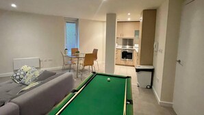 Un espacio habitable compacto con mesa de billar, sofá, comedor y kitchenette.
