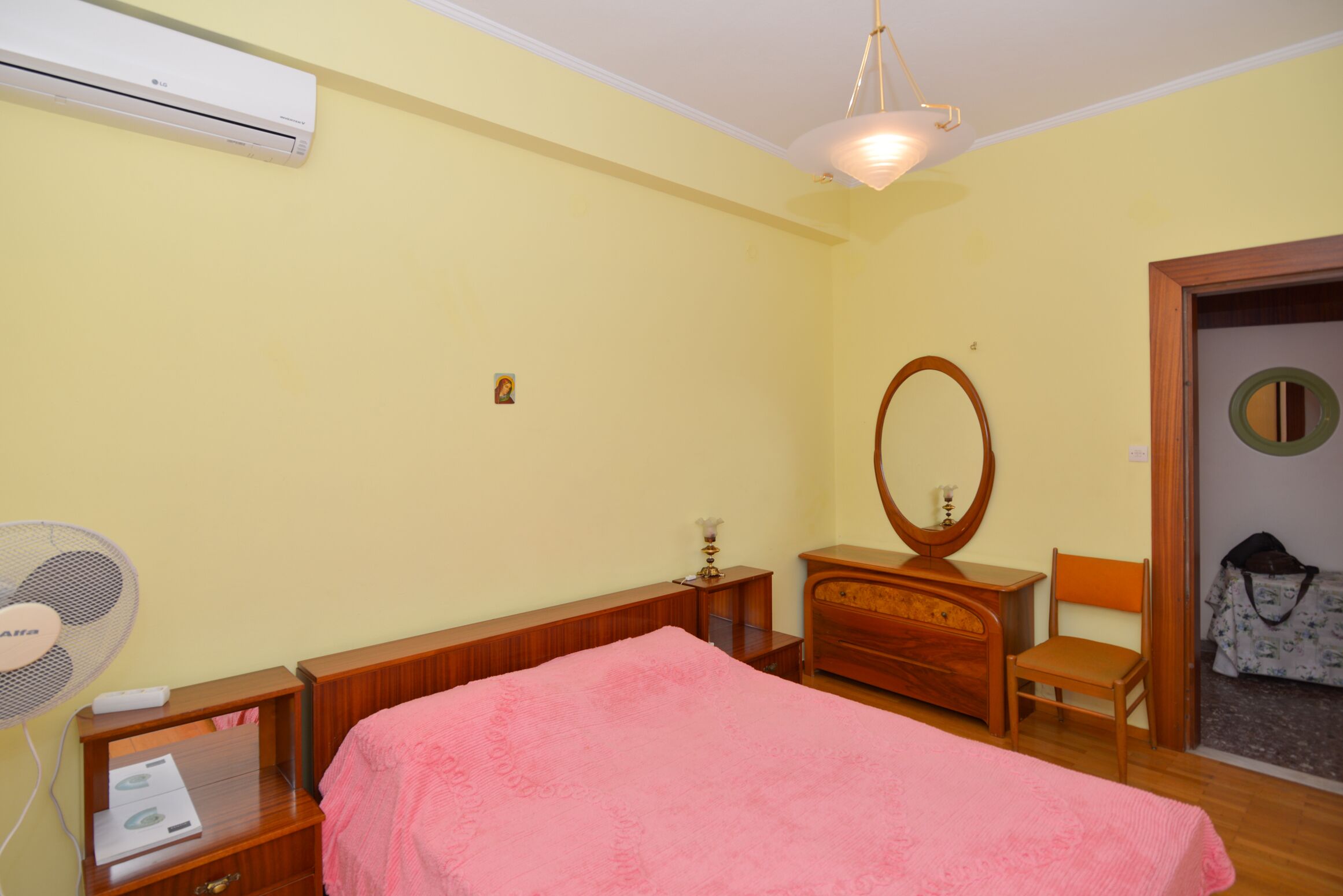 Un dormitorio con cama, cómoda de madera, silla y ventilador.