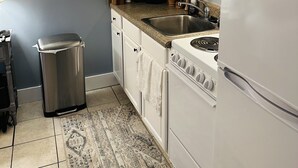 A kitchen with white cabinets, a stainless steel trash can, a microwave, and a stove. - Cute Condo close to Coligny Beach (Hilton Head Island)