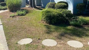 A two-story house with a brown roof and a blue exterior wall. There is a tree in front of the house and a circular garden bed with a hedge. - Cute Condo close to Coligny Beach (Hilton Head Island)