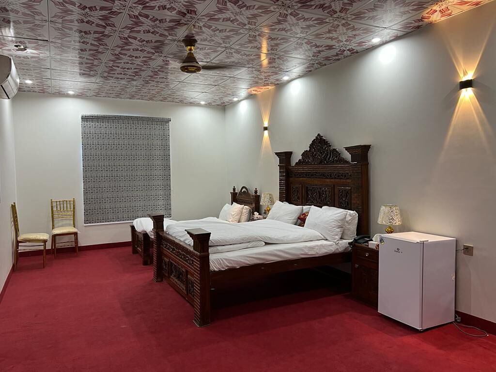 A bedroom with a wooden bed, a small white cabinet, a red carpet, and a ceiling with a patterned design.