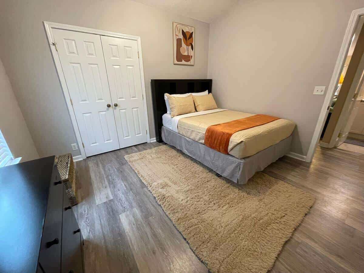 A bedroom with a bed, a dresser, a rug, and a door.