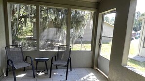 A covered patio with two chairs and a small table, large windows with views of trees and a yard, and a tiled floor. - Comfortable Coastal 2 BDRM home - 5 mins to downto (saint marys)