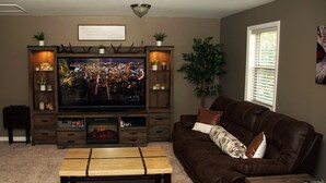 Ein Wohnzimmer mit Flachbildfernseher, einer Holz-Unterhaltungseinrichtung, einem braunen Ledersofa und einem Couchtisch.