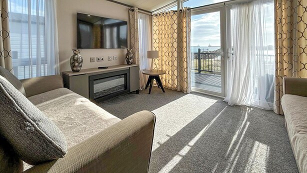 A hotel room with a sofa, a TV, a small table, and a balcony with curtains. - 2 bedroom accommodation in Peterhead (Peterhead)
