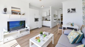 Una sala moderna con una televisión de pantalla plana, una mesa de comedor con sillas, un sof á y una zona de cocina al fondo.