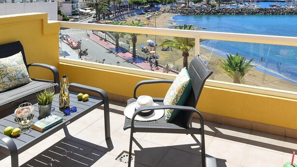 Un balcón con vista al mar, una mesa con una planta y una silla.