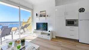 Una cocina moderna con televisor, gabinetes blancos y vista al mar.