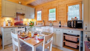 A wooden cabin kitchen with a dining table set, wooden cabinets, and a built-in microwave. - 2 bedroom accommodation in Garnant Ammanford (Garnant Ammanford)