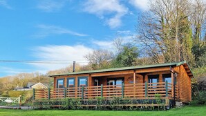 A wooden cabin with a balcony, surrounded by greenery and trees. - 2 bedroom accommodation in Garnant Ammanford (Garnant Ammanford)