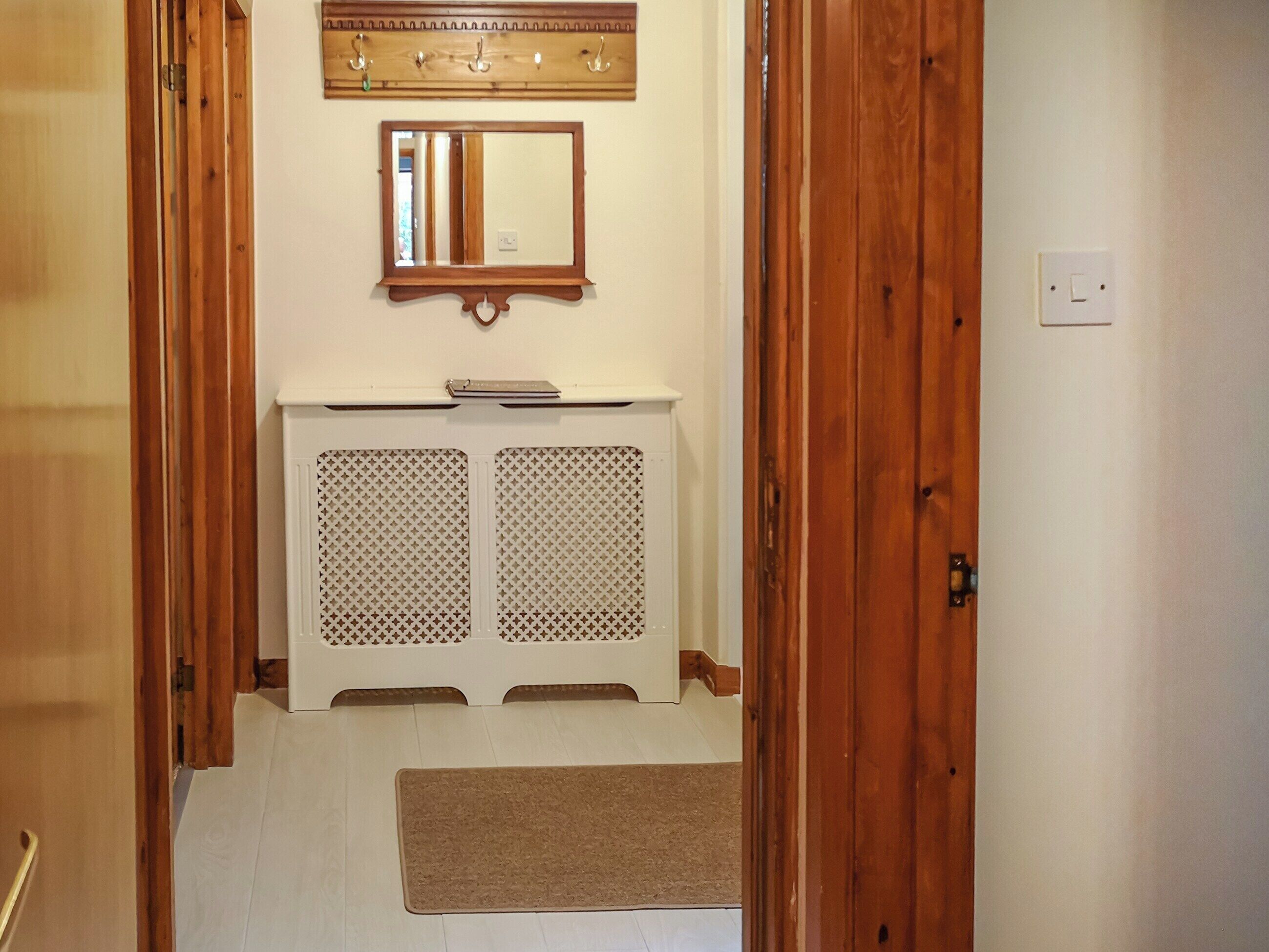 A hallway with a wooden door, a white radiator, a mirror, and a small shelf.