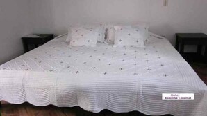 A single-bed room with a white bedspread featuring a bird pattern, two bedside tables, and a plain wall. - Hotel Esquina Colonial (Villa de Leyva)