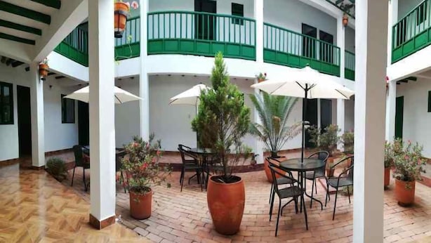 A covered courtyard with a tiled floor, outdoor seating area with tables and chairs, potted plants, and a green railing on the upper level. - Hotel Esquina Colonial (Villa de Leyva)