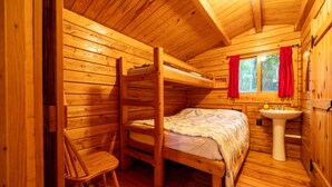 Ein Holzblockhauszimmer mit Etagenbetten, einem Waschbecken und einem Fenster mit Vorhängen.