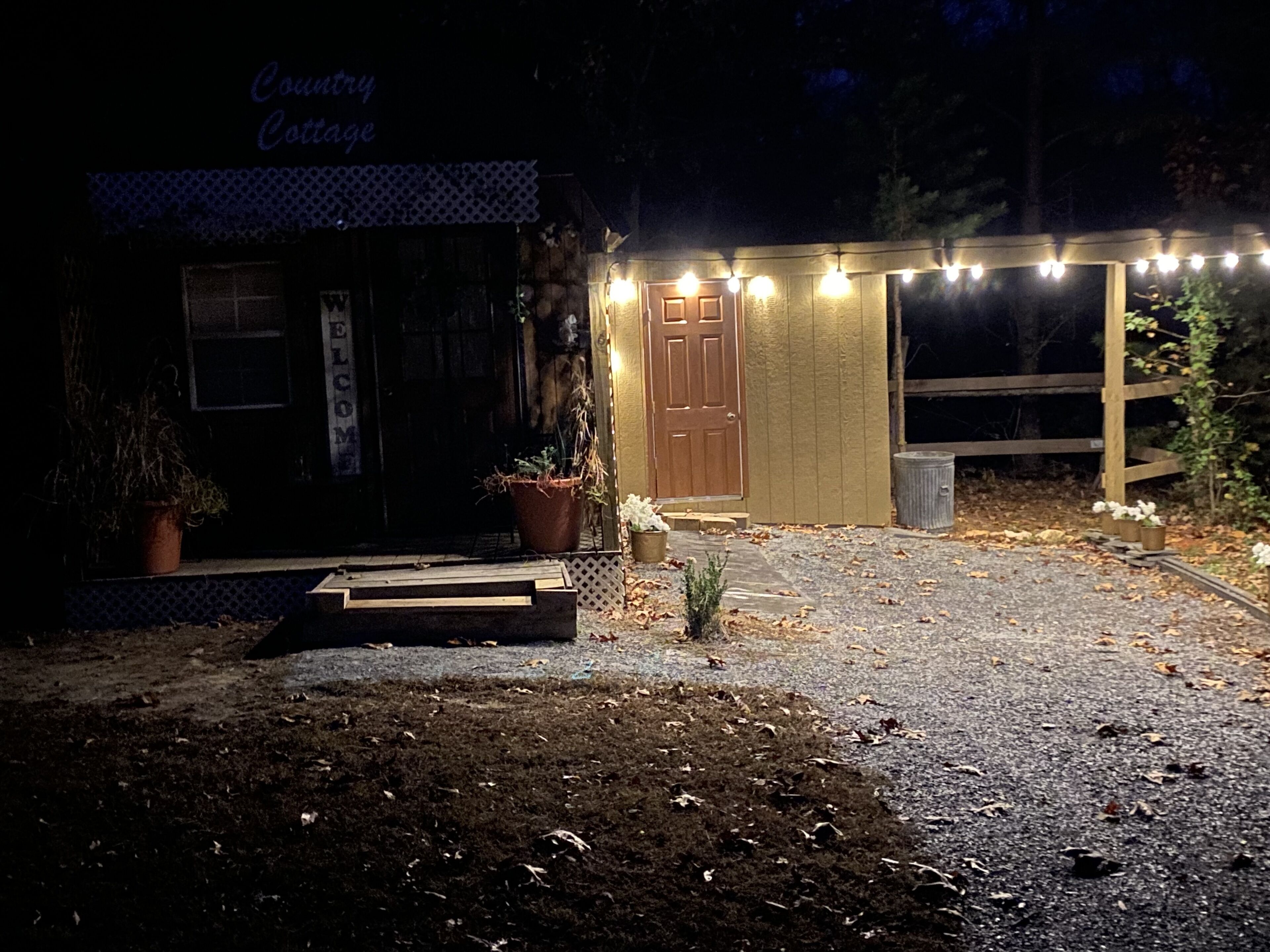Un edificio rústico con un letrero que dice 'Country Cottage', una puerta de madera y luces de cuerda.
