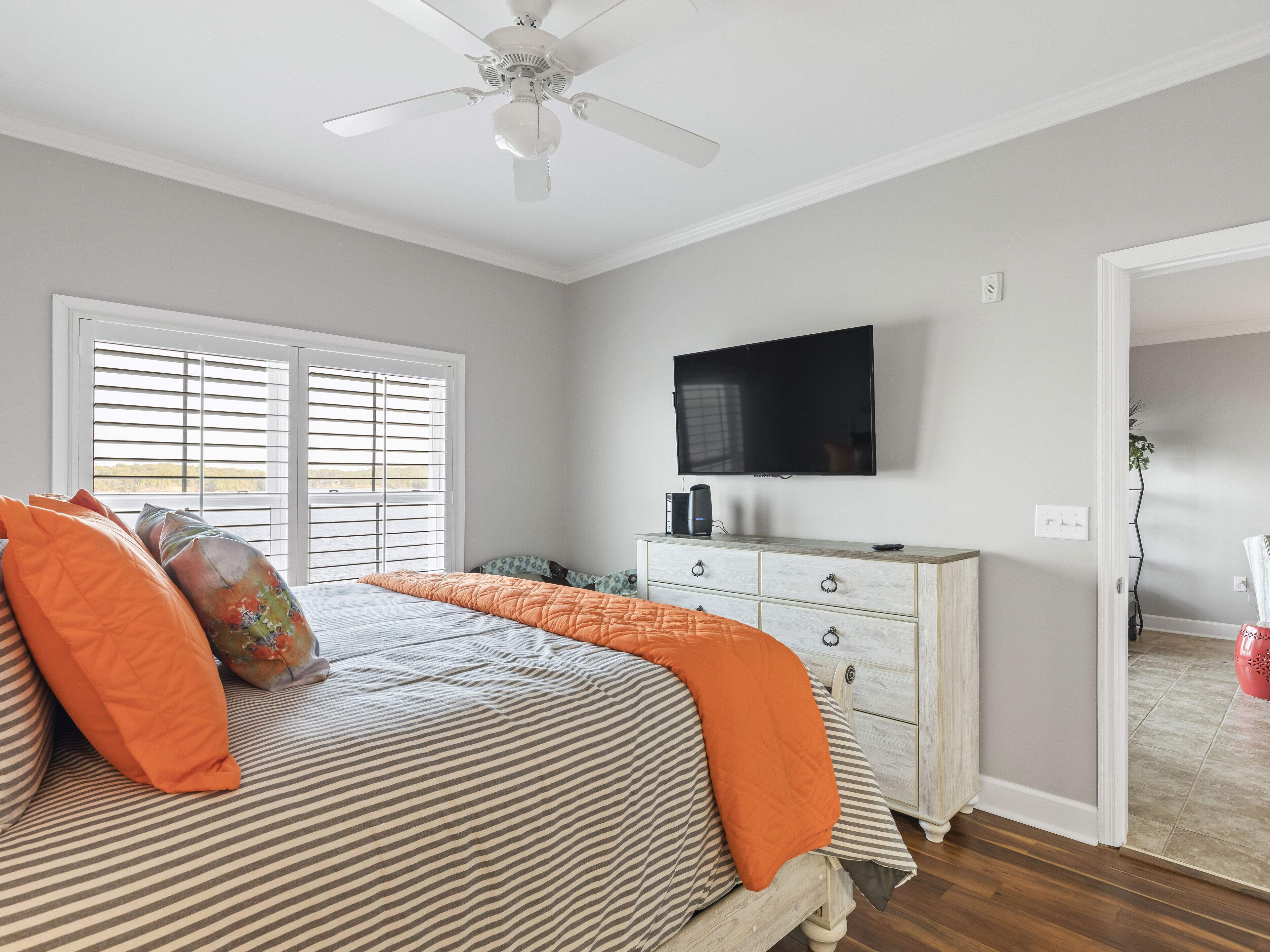 A bedroom with a bed, a dresser, a television, and a ceiling fan.