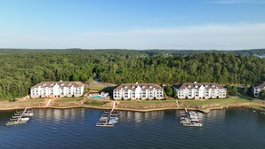 A lakeside resort with multiple white buildings, a dock with boats, and a forested backdrop.