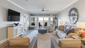 A spacious living room with a large TV, comfortable seating, and a view to the outside.