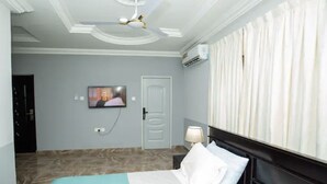 Une chambre d’hôtel avec un lit, un téléviseur fixé au mur, un ventilateur de plafond et une fenêtre avec des rideaux.