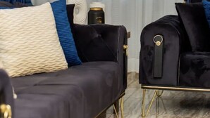 Une pièce comprenant un canapé de couleur sombre, un fauteuil assorti et une petite table sur laquelle se trouvent une bouteille et un récipient.