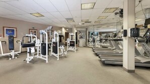 Une salle de sport équipée de tapis de course, d’appareils de musculation et d’un mur entièrement recouvert de miroirs.