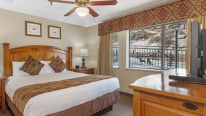 Une chambre d’hôtel avec un lit en bois, un bureau, un ventilateur de plafond et une fenêtre donnant sur un paysage montagneux.