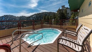 Un bain à remous sur une terrasse en bois, avec vue sur une chaîne de montagnes boisées.