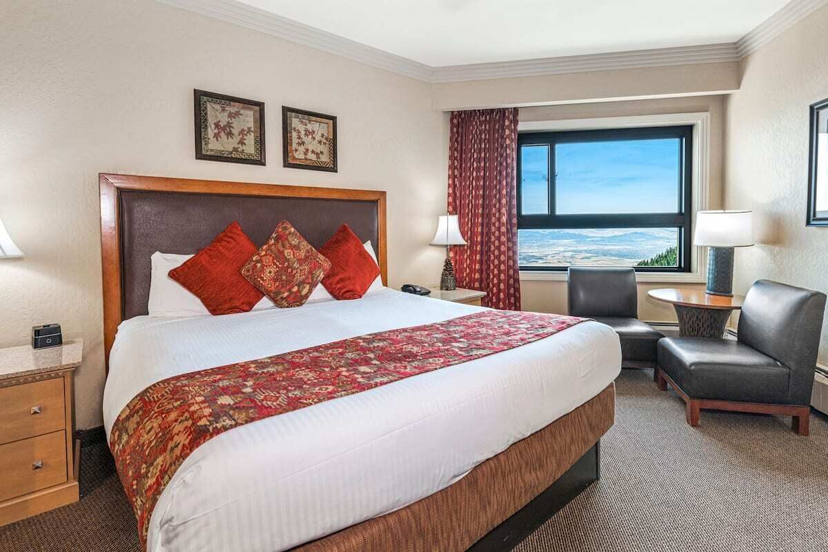A hotel room with a large bed, a desk, a chair, and a view of the outdoors.