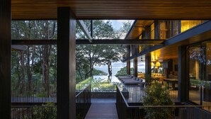 A modern building with a wooden deck leading to a balcony overlooking a forested area.