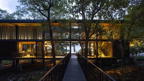 A modern building with a wooden deck leading to a glass entrance, surrounded by trees.
