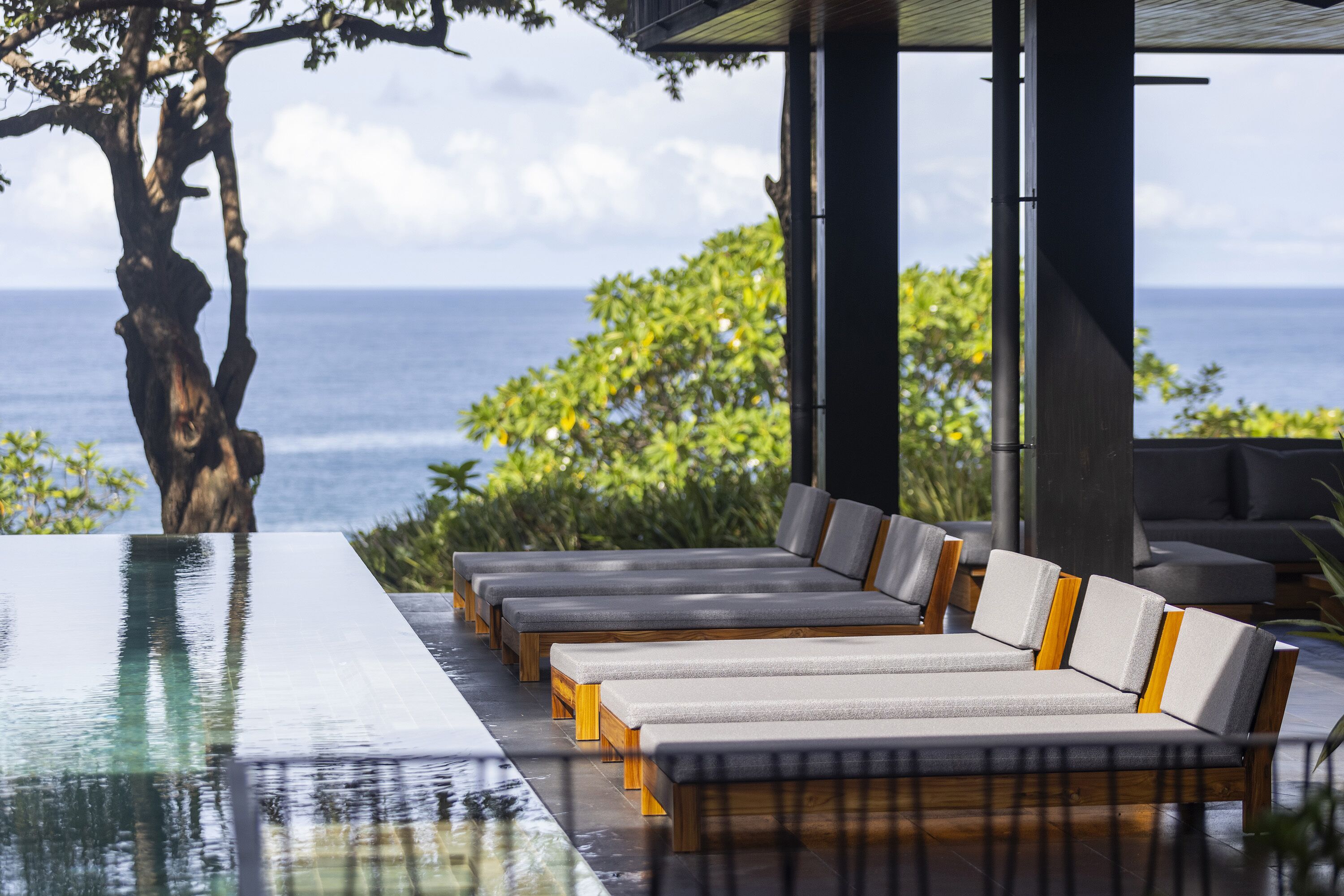 Un área junto a la piscina con sillones de descanso y vista al océano.