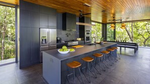 A modern kitchen with a large island, bar stools, and a view of the outdoors.