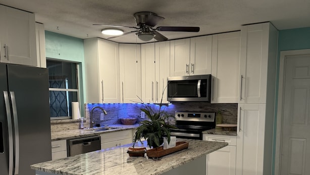 A modern kitchen with white cabinets, a granite countertop, a stainless steel refrigerator, a microwave, and a stove.