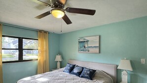 A bedroom with a bed, a ceiling fan, a nightstand, a lamp, and a window with curtains.