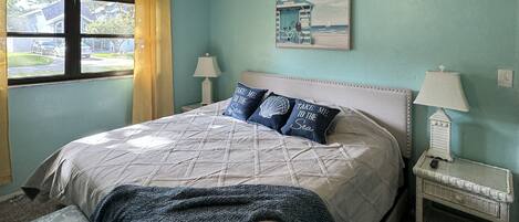 Un dormitorio con cama, ventilador de techo, mesita de noche, lámpara y ventana con cortinas.