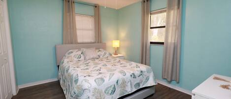 A bedroom with a bed, a ceiling fan, a nightstand with a lamp, and a dresser.
