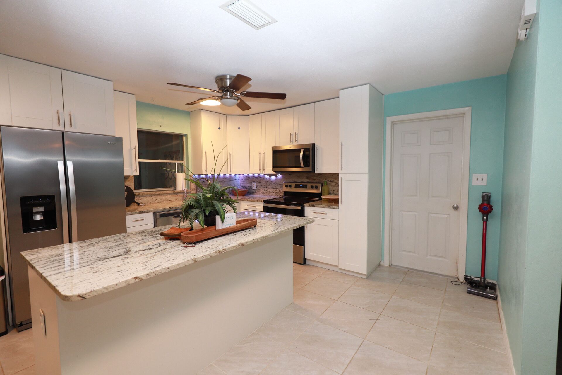 A kitchen with white cabinets, a stainless steel refrigerator, a microwave, and a ceiling fan.